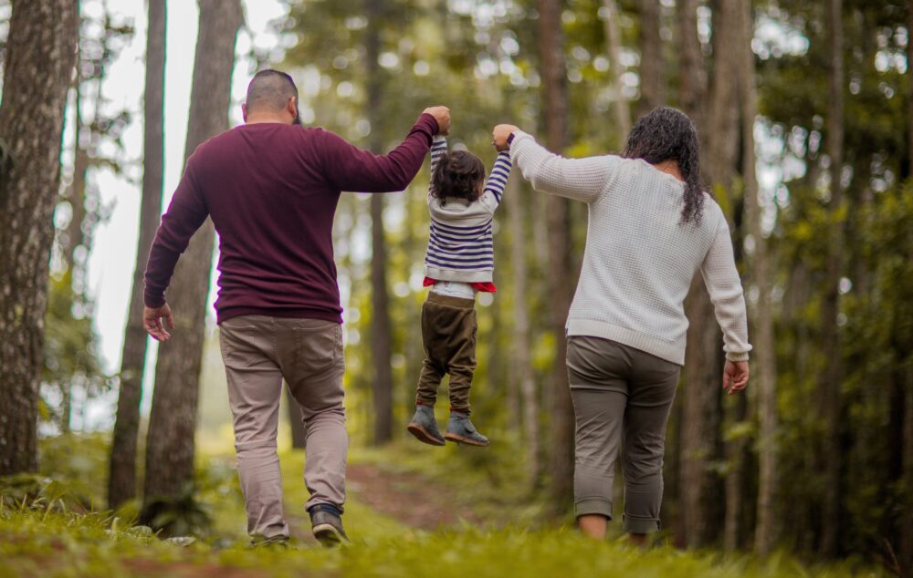 Parents swinging their child between them while walking through a forest