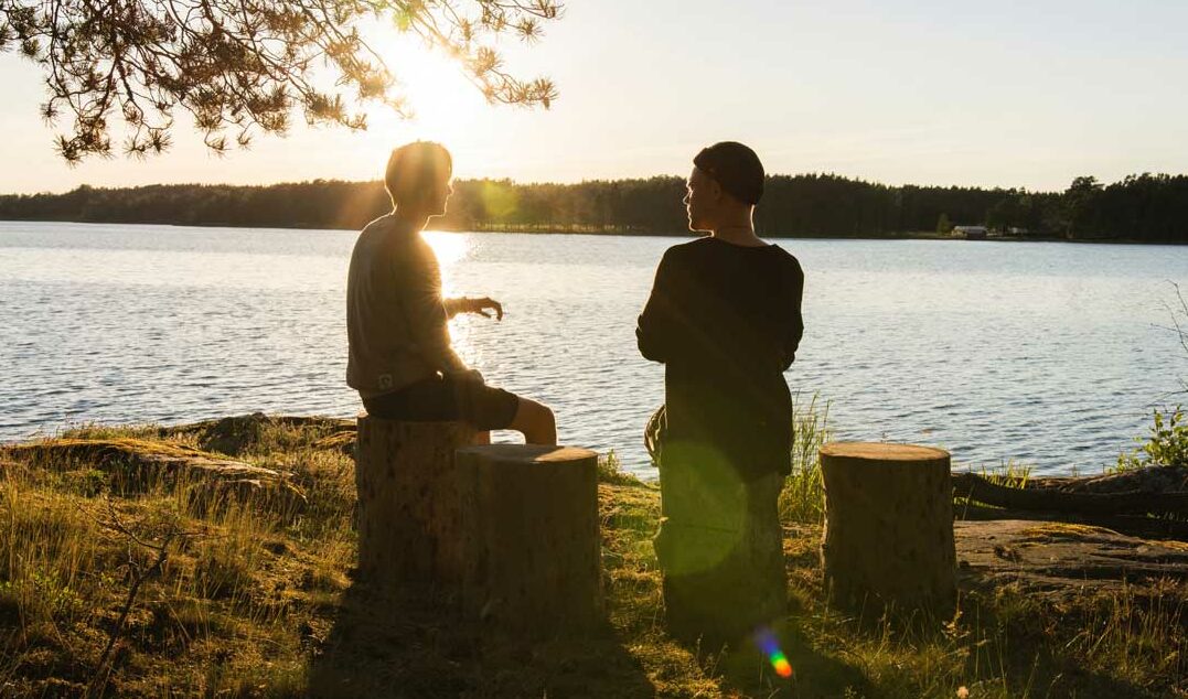 two men sitting by a lake at sunset