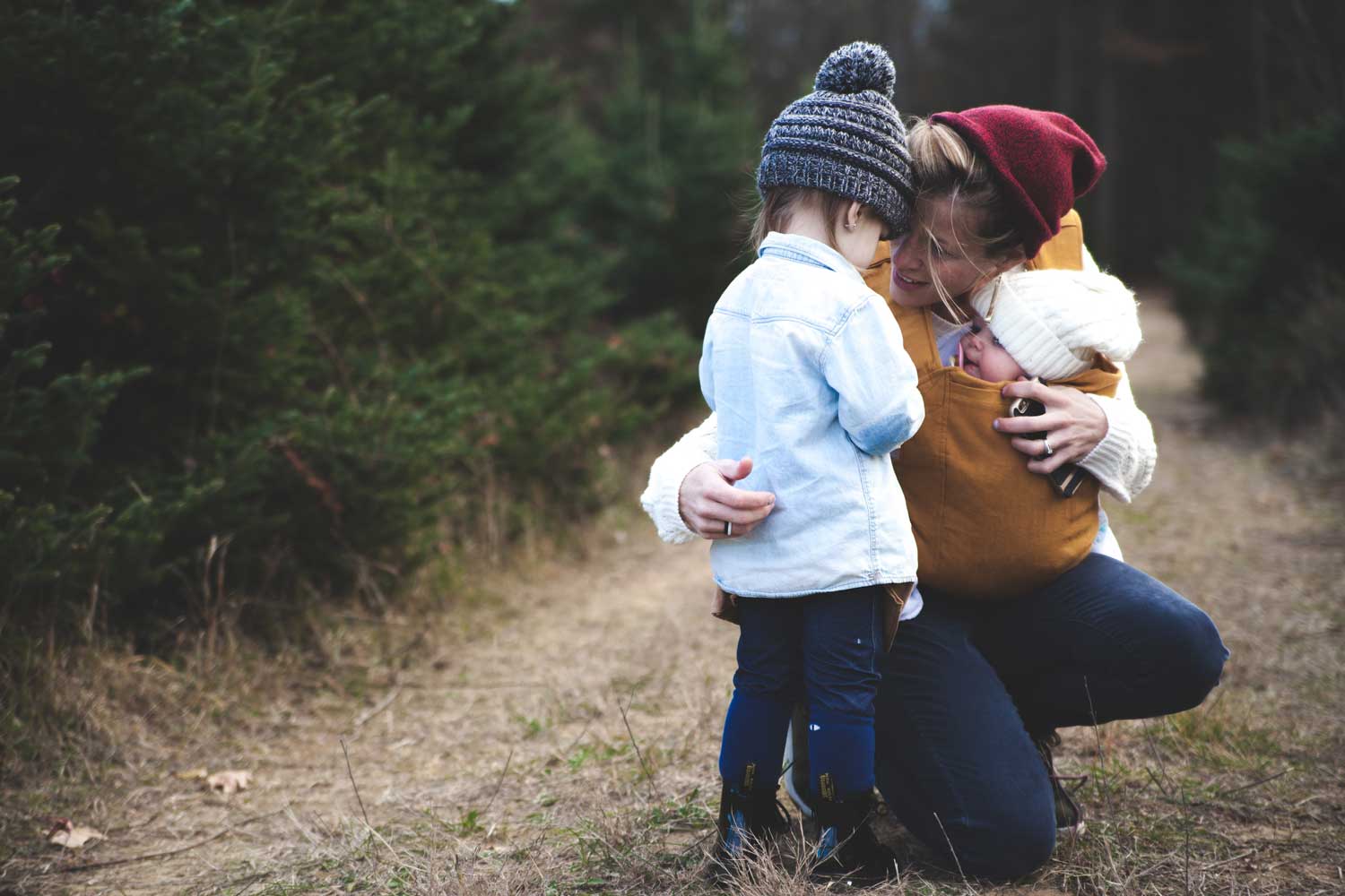 Woman crouching on a woodland path, holding two children