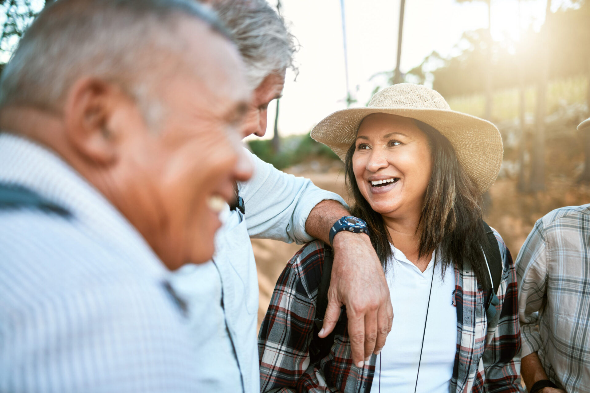 Happy senior woman in nature with friends while taking an outdoor walk in spring. Smiling mature woman having a conversation with a man outside. Old smiling lady having fun while hiking with aged men.