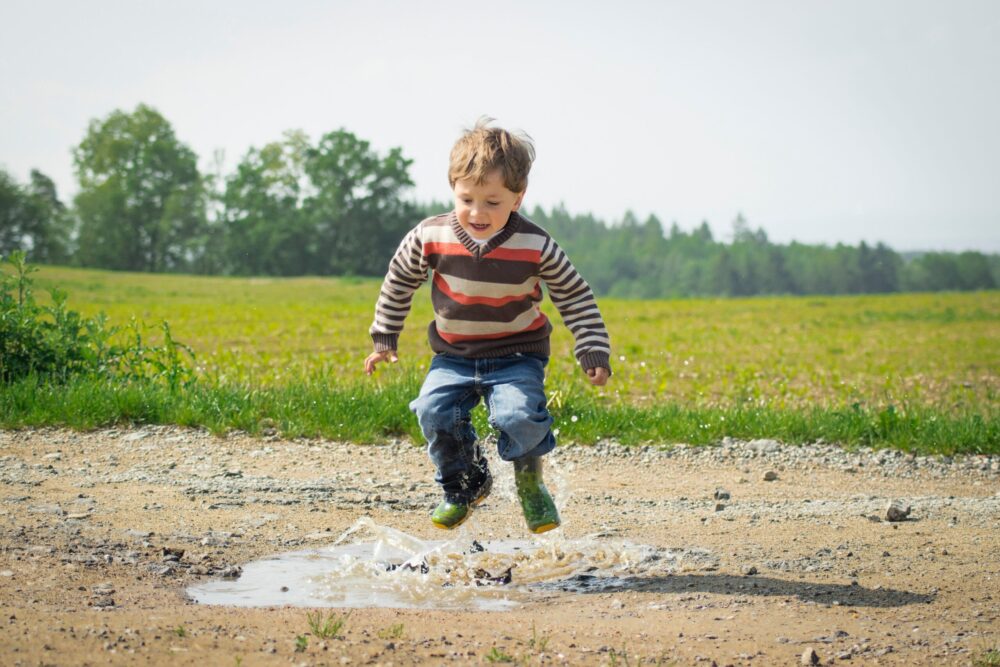 Child in wellington boots splashing in a puddle on a country path