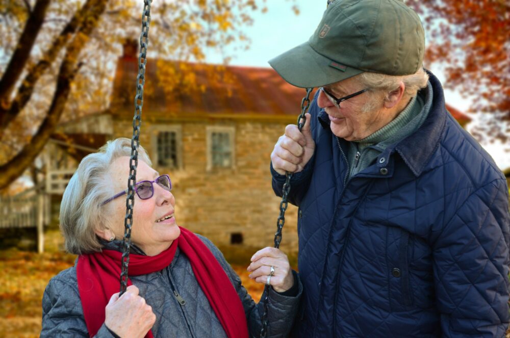 Older couple sitting together on a swing in autumn, smiling at each other