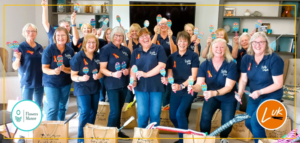 17 of the Sparkly Singers stood in a room smiling and holding paper maracas 