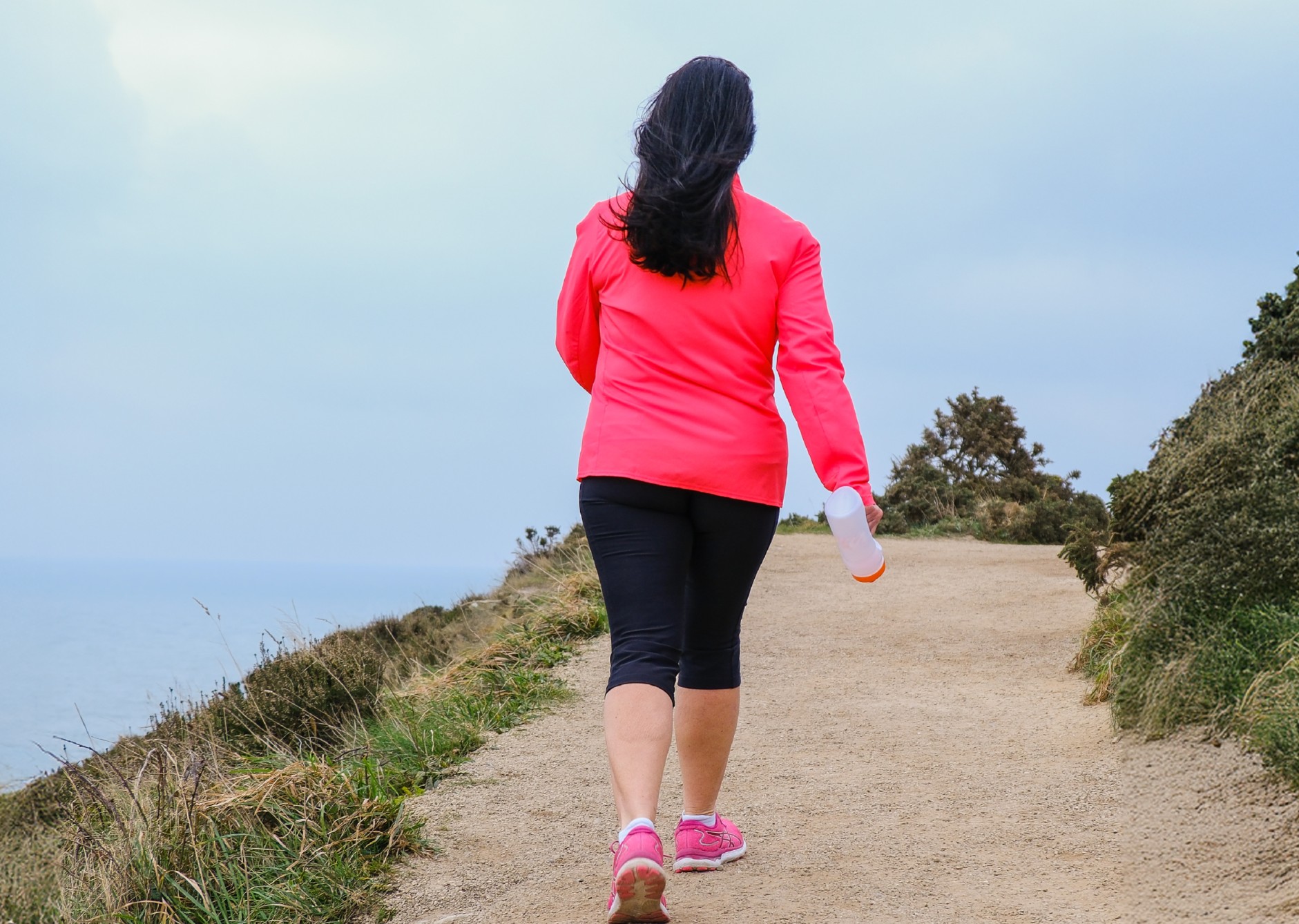 Lady in pink top and sport gear walking away from camera along a track