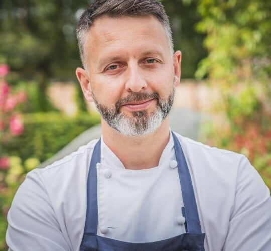 Mark stood in a garden in chef whites and blue apron