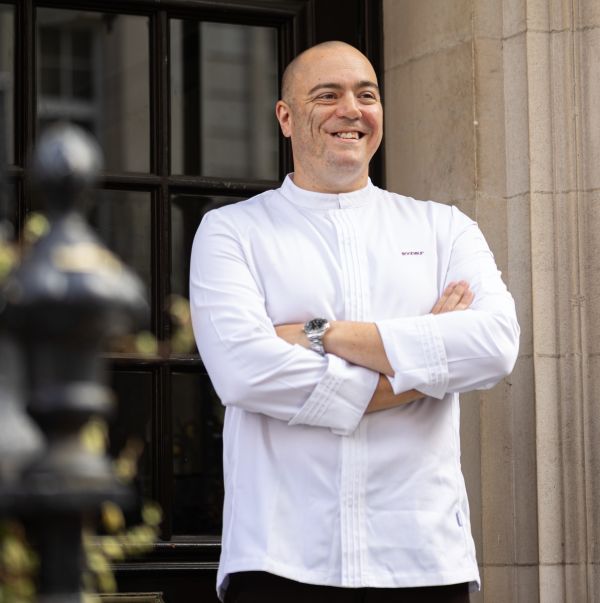 Matt Abe in chef whites stood outside cross armed - Leukaemia UK Who's Cooking Dinner?