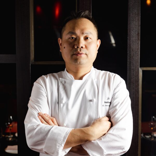 Michael Zhen in chef whites cross armed in a dark dinning room
